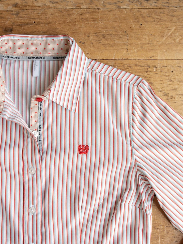 The Savannah Sevens western life{&}style Patton Striped Tencel Performance Shirt is a women’s long sleeve button up, featuring red, white, and teal stripes. Laid flat on a wooden surface, the shirt displays a red embroidered logo on the chest and contrasting dotted fabric inside the collar.