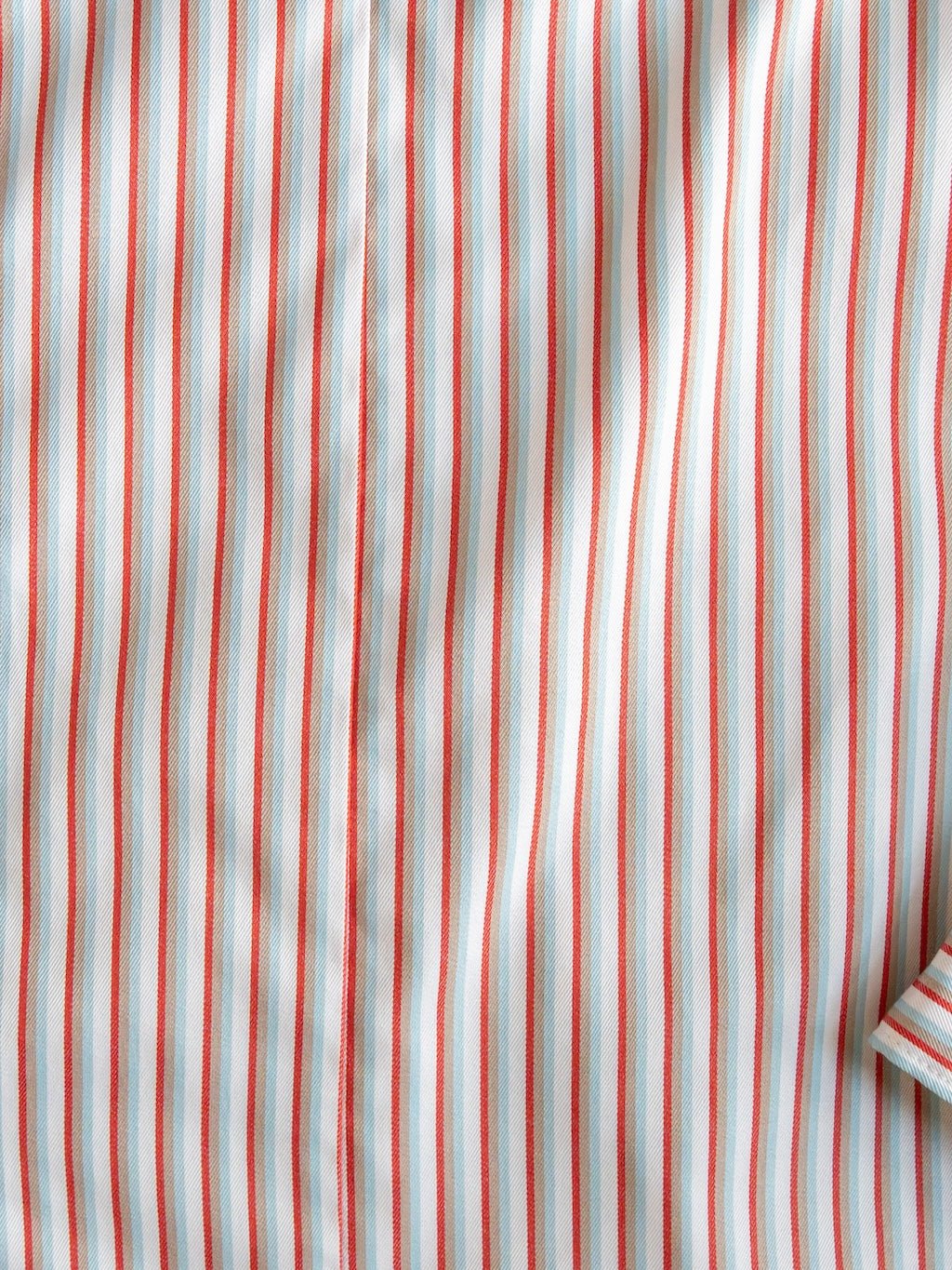 A close-up of the Patton Striped Tencel Performance Shirt by Savannah Sevens western life{&}style, showcasing its vertical red, white, and light blue stripes on a long sleeve tencel blend fabric. A small folded edge of the shirt appears in the bottom right corner.