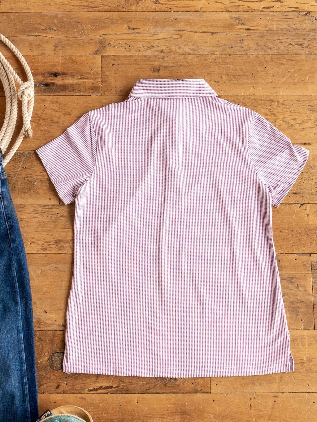 The Payden Burgundy Striped Polo by Savannah Sevens western life{&}style, made with stretchy fabric for comfort, is laid flat next to blue jeans, tan shoes, and a coiled rope on a wooden floor.