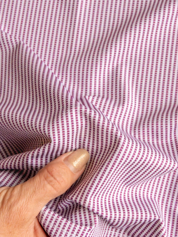 A hand with painted nails bunches up the Payden Burgundy Striped Polo from Savannah Sevens western life{&}style, showing off its small purple and white striped fabric.
