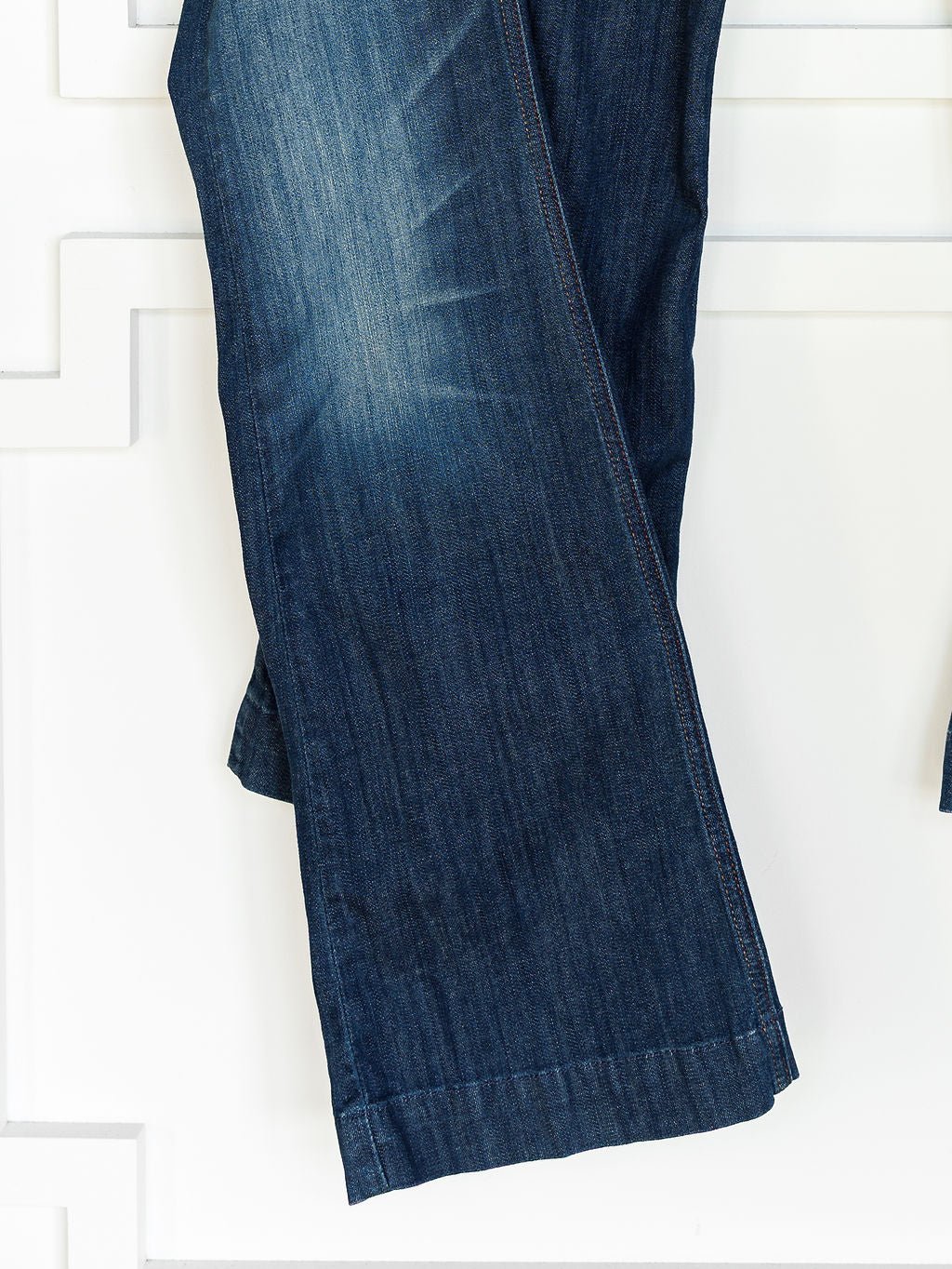 A close-up of Ariat's The Payson Perfect Rise Slim Trouser Jean in medium dark wash with subtle fading and seam details, displayed against a white background with a geometric pattern.