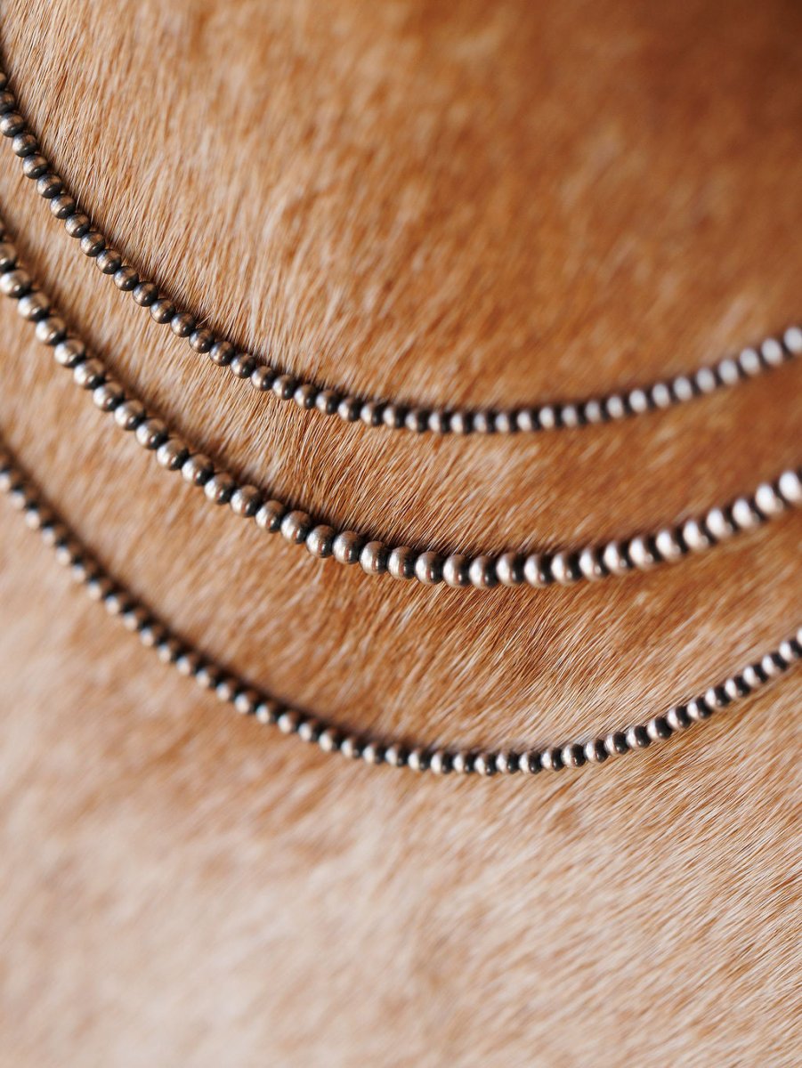 Close-up of three Pecos Necklaces by Savannah Sevens western life{&}style, featuring sterling silver beaded chains hand strung and arranged in curved parallel lines on a textured light brown furry surface.