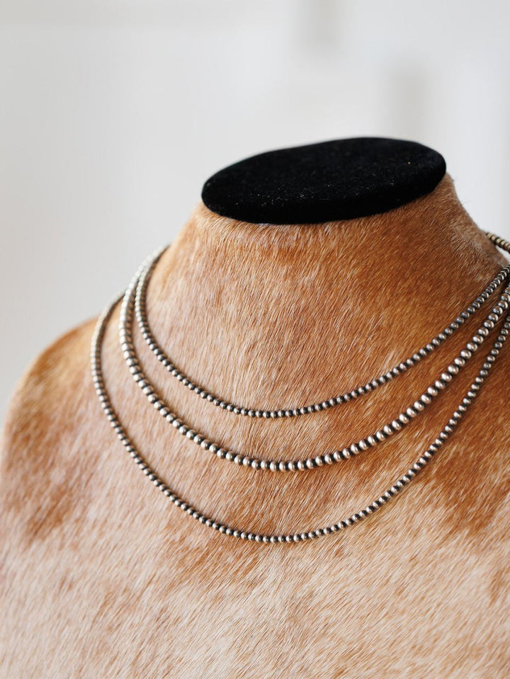 The Pecos Necklace by Savannah Sevens western life{&}style features three sterling silver layers, including a hand-strung Navajo pearl strand, displayed on a tan fur-textured bust with black top, set against a softly blurred white background.