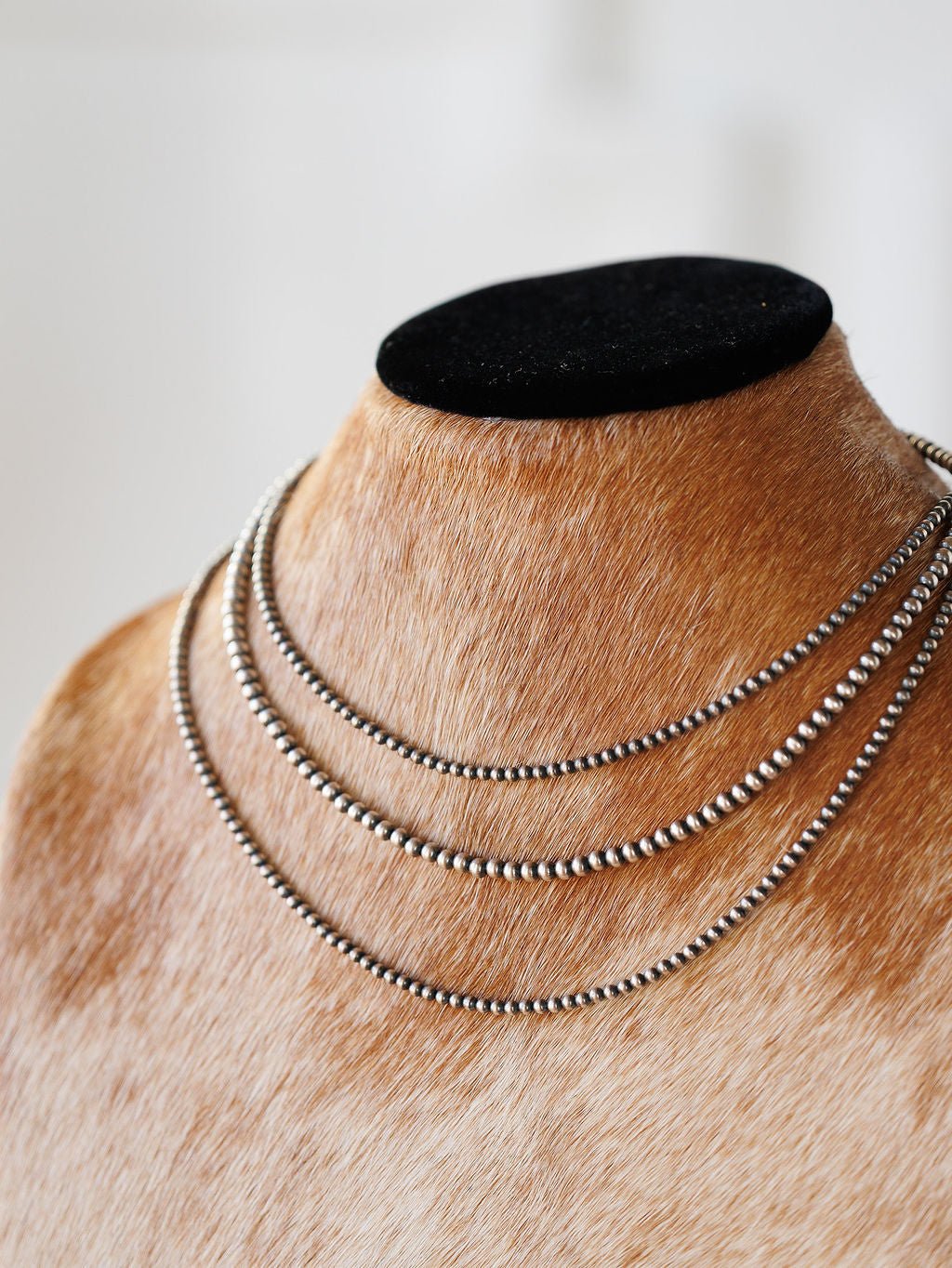 The Pecos Necklace by Savannah Sevens western life{&}style features three sterling silver layers, including a hand-strung Navajo pearl strand, displayed on a tan fur-textured bust with black top, set against a softly blurred white background.