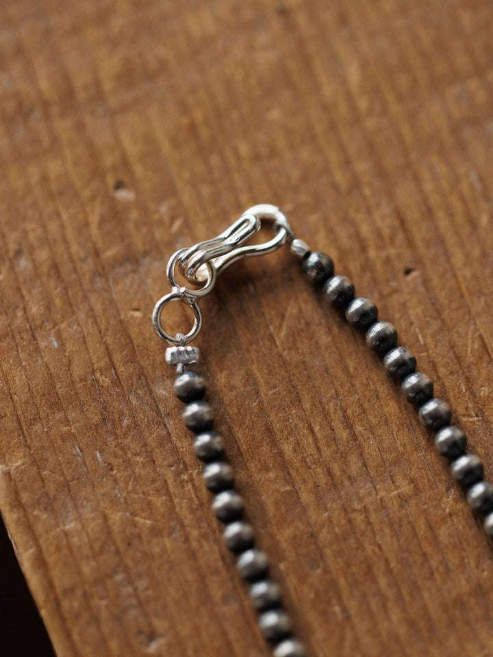 Close-up of the Pecos Necklace by Savannah Sevens western life{&}style, a hand-strung piece with alternating dark and light beads and a sterling silver hook-and-ring clasp, shown on a wooden surface.