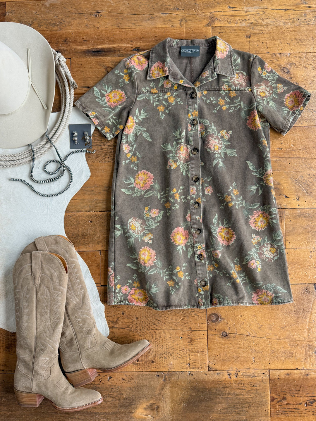 The Petaluma Floral Button Up Dress by Savannah Sevens western life{&}style, paired with beige cowboy boots, a white wide-brim hat, a silver necklace, and a white top, arranged on a wooden floor.