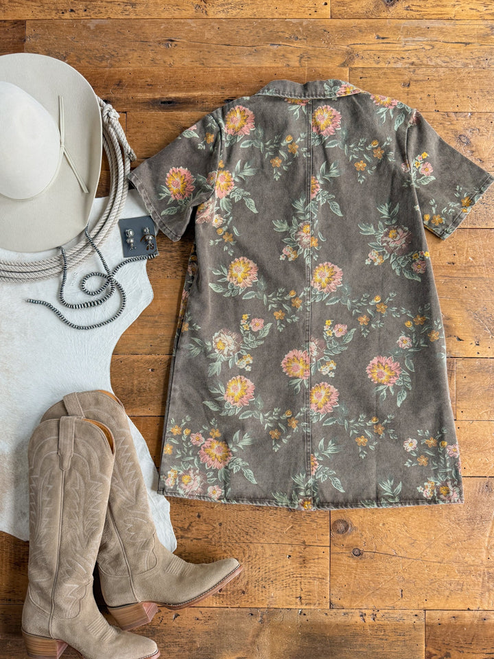 The Petaluma Floral Button Up Dress by Savannah Sevens western life{&}style is laid on a wood floor alongside a white cowboy hat, coiled necklace, white cowhide rug, and tan cowboy boots.