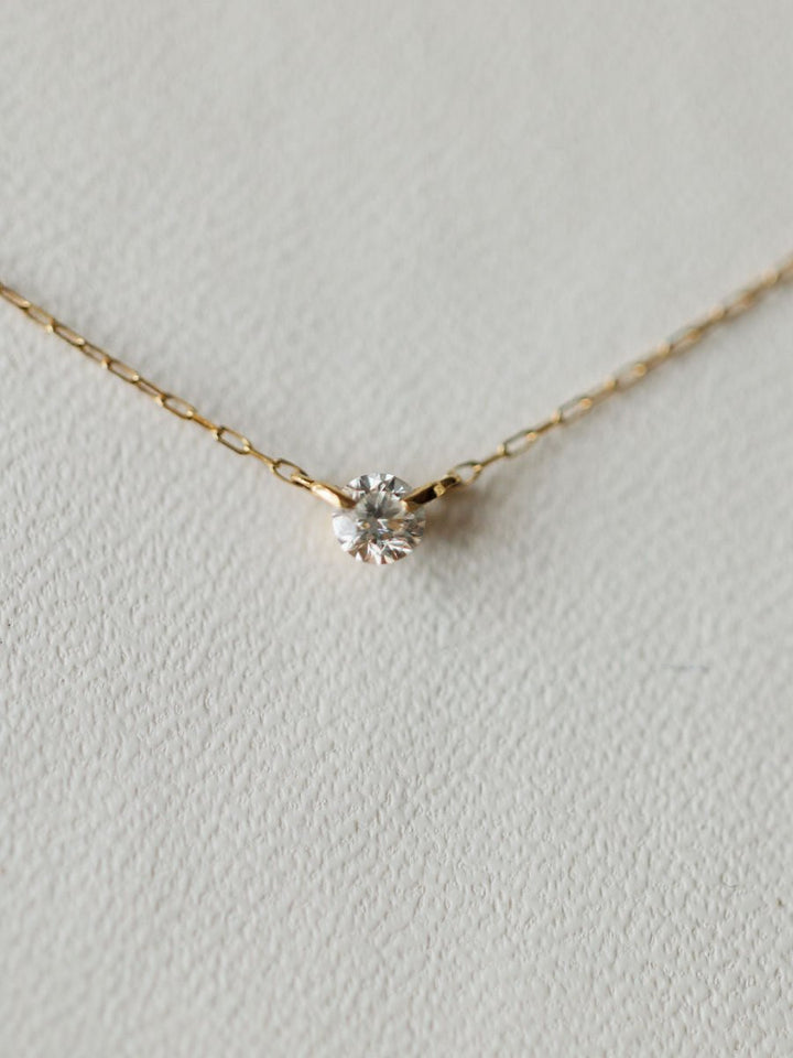 The Petite Diamond Necklace {Gold} by Savannah Sevens western life{&}style showcases a bezel set diamond pendant in 18K yellow gold, displayed on a light textured surface.