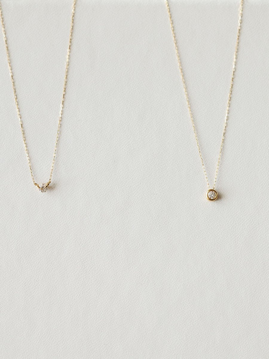Two delicate gold necklaces by Savannah Sevens western life{&}style rest on a light, textured surface. The left is the Petite Diamond Necklace {Gold}; the right showcases a round, bezel-set diamond pendant.