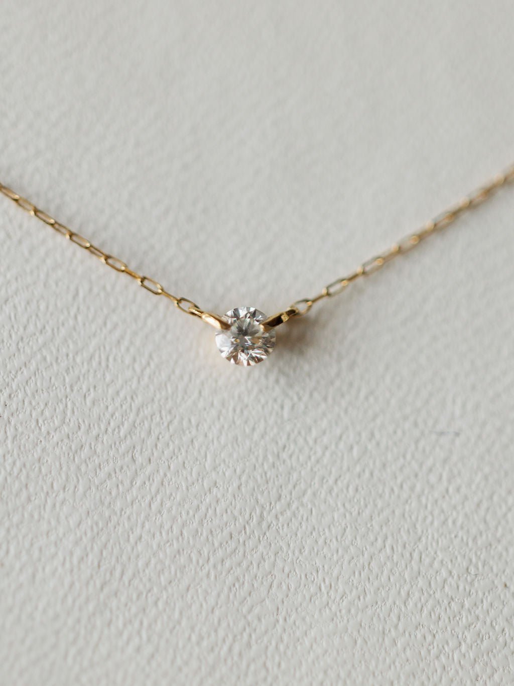The Petite Diamond Necklace {Gold} by Savannah Sevens western life{&}style showcases a bezel set diamond pendant in 18K yellow gold, displayed on a light textured surface.