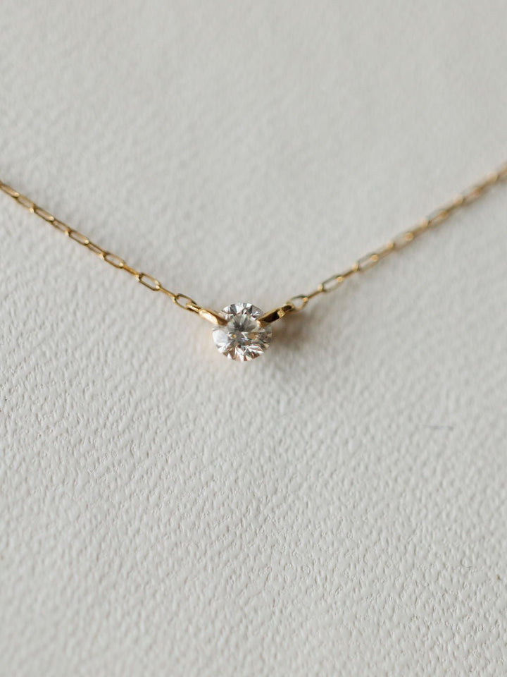 The Petite Diamond Necklace {Gold} by Savannah Sevens western life{&}style showcases a bezel set diamond pendant in 18K yellow gold, displayed on a light textured surface.