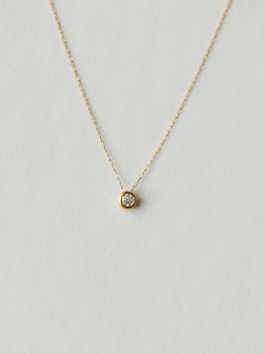 The Petite Diamond Necklace {Gold} by Savannah Sevens western life{&}style features a small round bezel-set diamond on an 18K yellow gold chain, shown against a light neutral background.