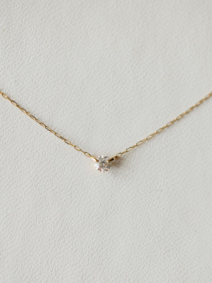 The Petite Diamond Necklace {Gold} by Savannah Sevens western life{&}style features an 18K yellow gold chain with a small, round bezel set diamond pendant, shown against a light, textured background.