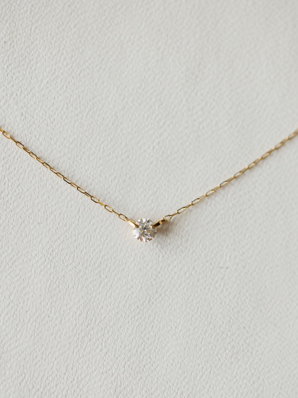 The Petite Diamond Necklace {Gold} by Savannah Sevens western life{&}style features an 18K yellow gold chain with a small, round bezel set diamond pendant, shown against a light, textured background.
