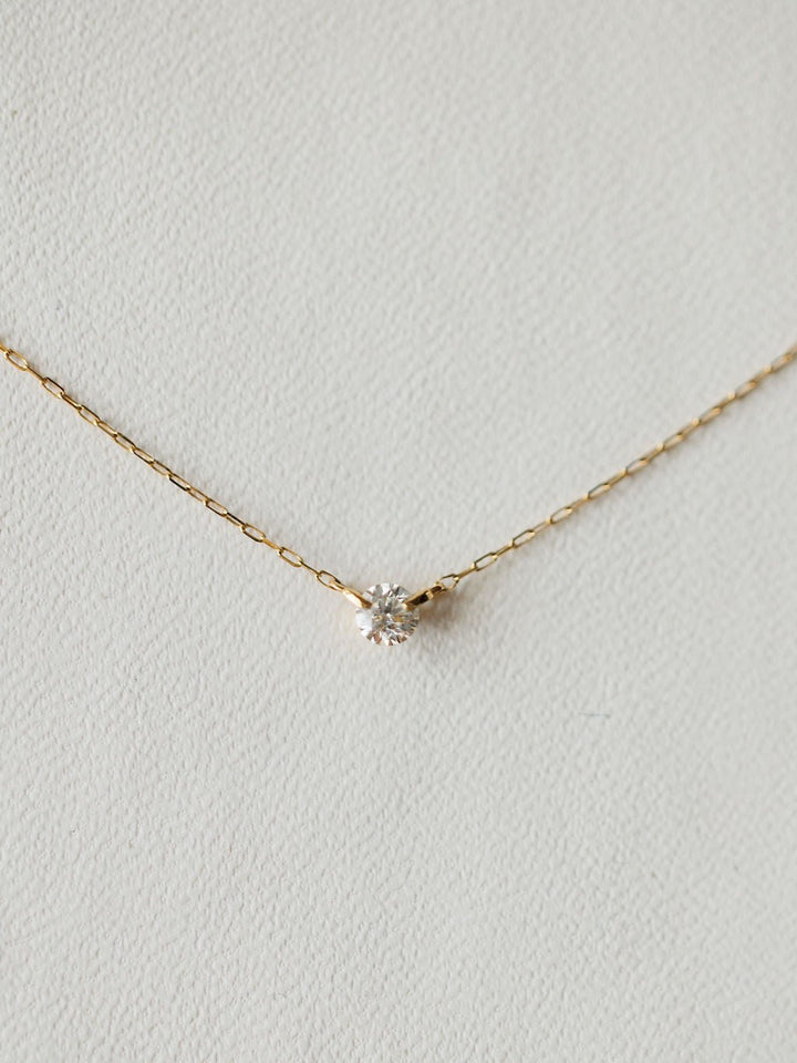 The Petite Diamond Necklace {Gold} by Savannah Sevens western life{&}style features an 18K yellow gold chain with a small, round bezel set diamond pendant, shown against a light, textured background.