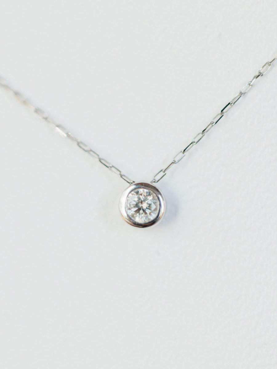 A close-up of the Petite Diamond Necklace {White Gold} by Savannah Sevens western life{&}style, featuring a delicate 18K white gold chain and a single natural round diamond solitaire pendant against a white background.