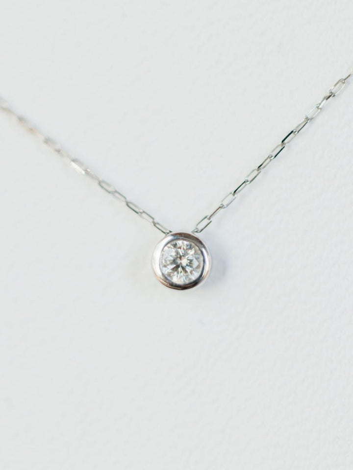 A close-up of the Petite Diamond Necklace {White Gold} by Savannah Sevens western life{&}style, featuring a delicate 18K white gold chain and a single natural round diamond solitaire pendant against a white background.