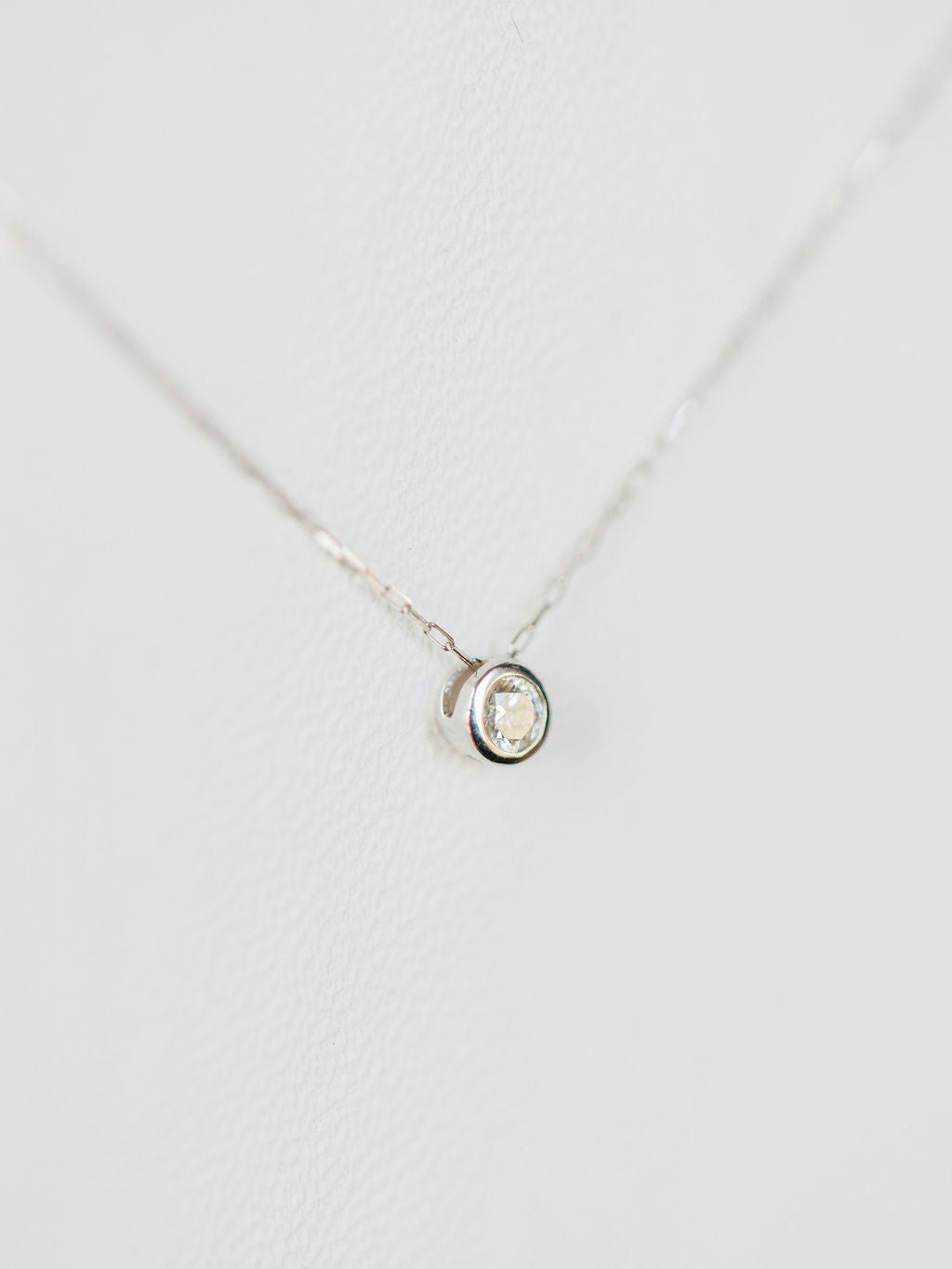 The Petite Diamond Necklace {White Gold} by Savannah Sevens western life{&}style features a small natural round diamond solitaire pendant in 18K white gold, displayed on a white background.