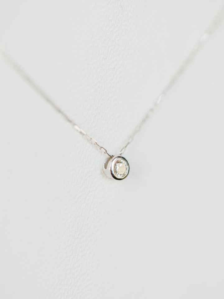 The Petite Diamond Necklace {White Gold} by Savannah Sevens western life{&}style features a small natural round diamond solitaire pendant in 18K white gold, displayed on a white background.