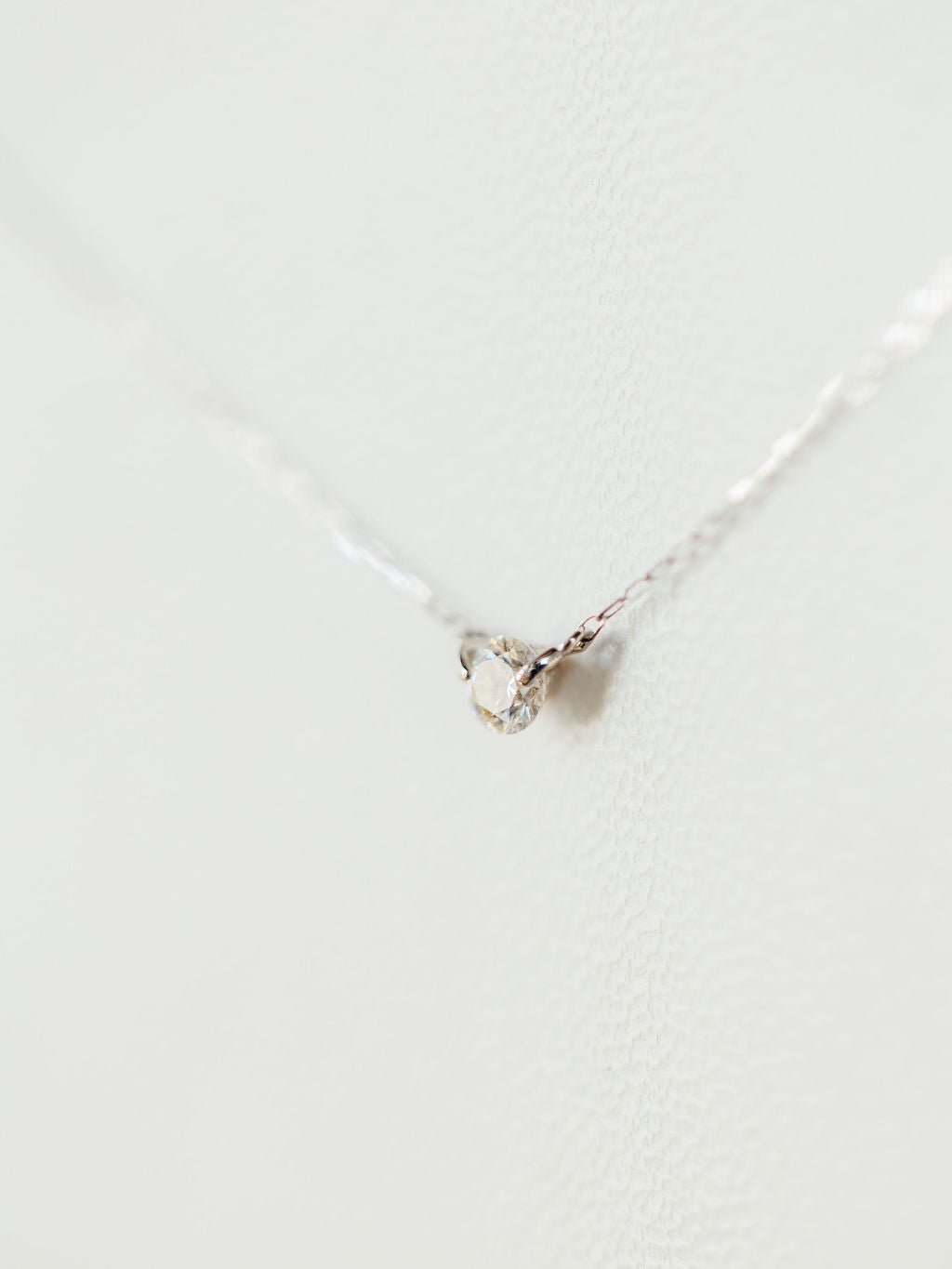 A close-up of the Petite Diamond Necklace {White Gold} by Savannah Sevens western life{&}style, featuring a delicate natural round diamond pendant, set against a softly textured white background.