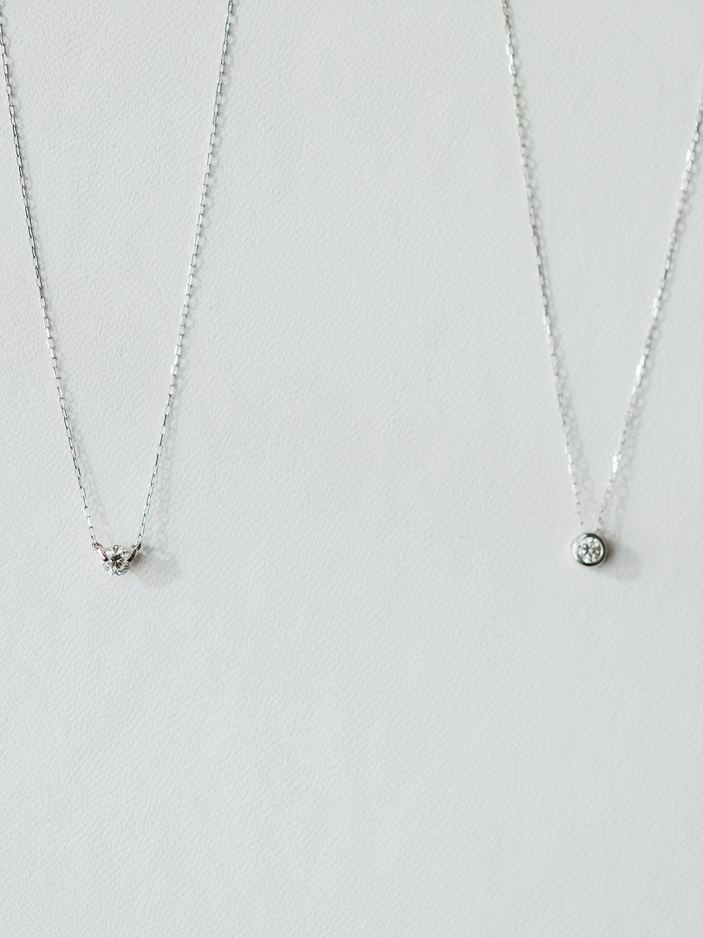 Two silver necklaces on a light background: the left has a small triangle pendant with stones, while the right is Savannah Sevens western life{&}style’s Petite Diamond Necklace in 18K white gold featuring a natural round diamond.