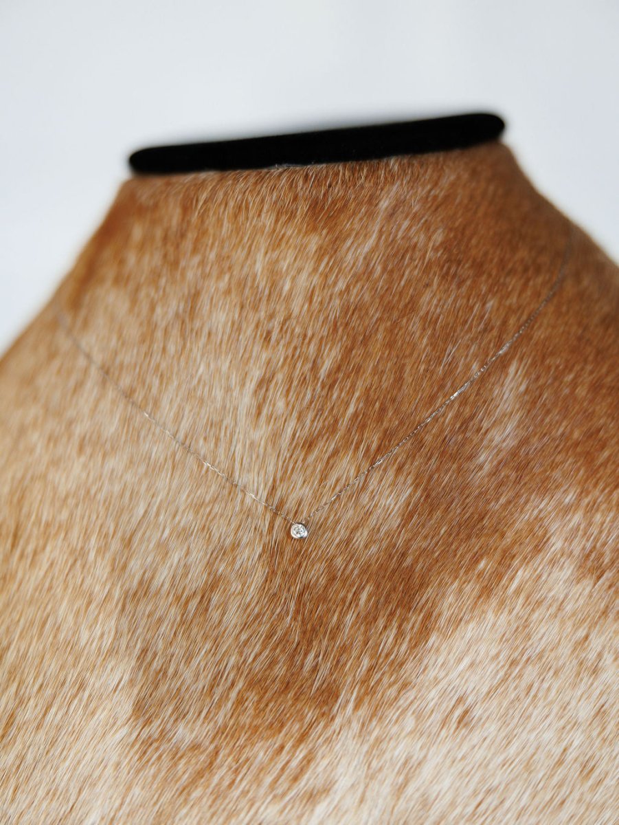 The Petite Diamond Necklace {White Gold} by Savannah Sevens western life{&}style, featuring a small natural round diamond, is shown on a tan and white cowhide bust stand with a black top.