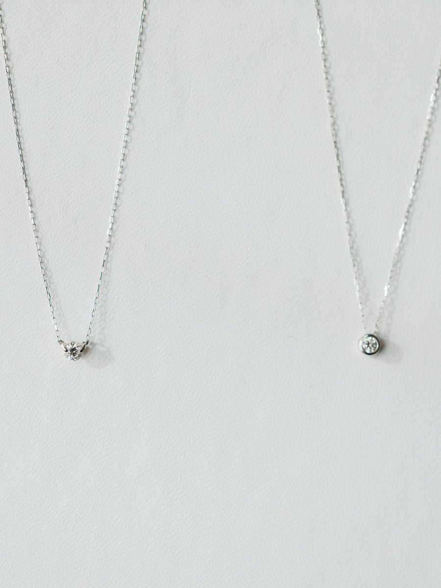 Two silver necklaces on a light background: the left has a small triangle pendant with stones, while the right is Savannah Sevens western life{&}style’s Petite Diamond Necklace in 18K white gold featuring a natural round diamond.