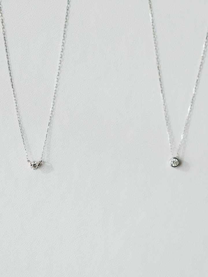 Two silver necklaces on a light background: the left has a small triangle pendant with stones, while the right is Savannah Sevens western life{&}style’s Petite Diamond Necklace in 18K white gold featuring a natural round diamond.