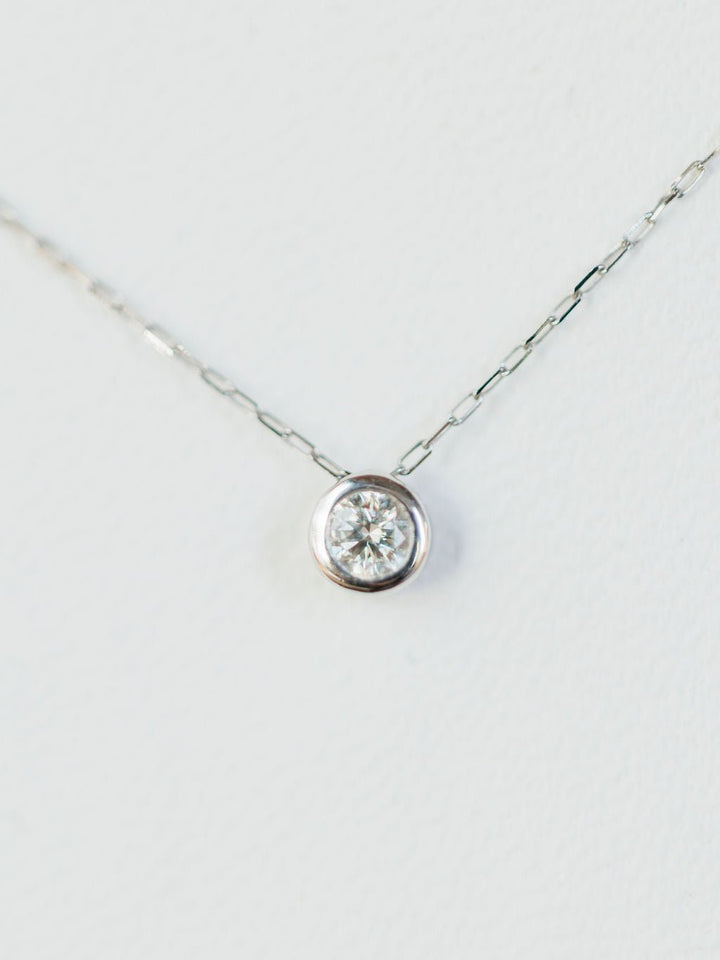 A close-up of the Petite Diamond Necklace {White Gold} by Savannah Sevens western life{&}style, featuring a delicate 18K white gold chain and a single natural round diamond solitaire pendant against a white background.