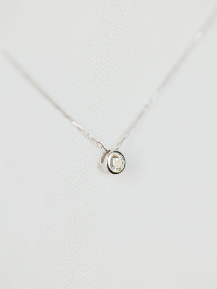 The Petite Diamond Necklace {White Gold} by Savannah Sevens western life{&}style features a small natural round diamond solitaire pendant in 18K white gold, displayed on a white background.