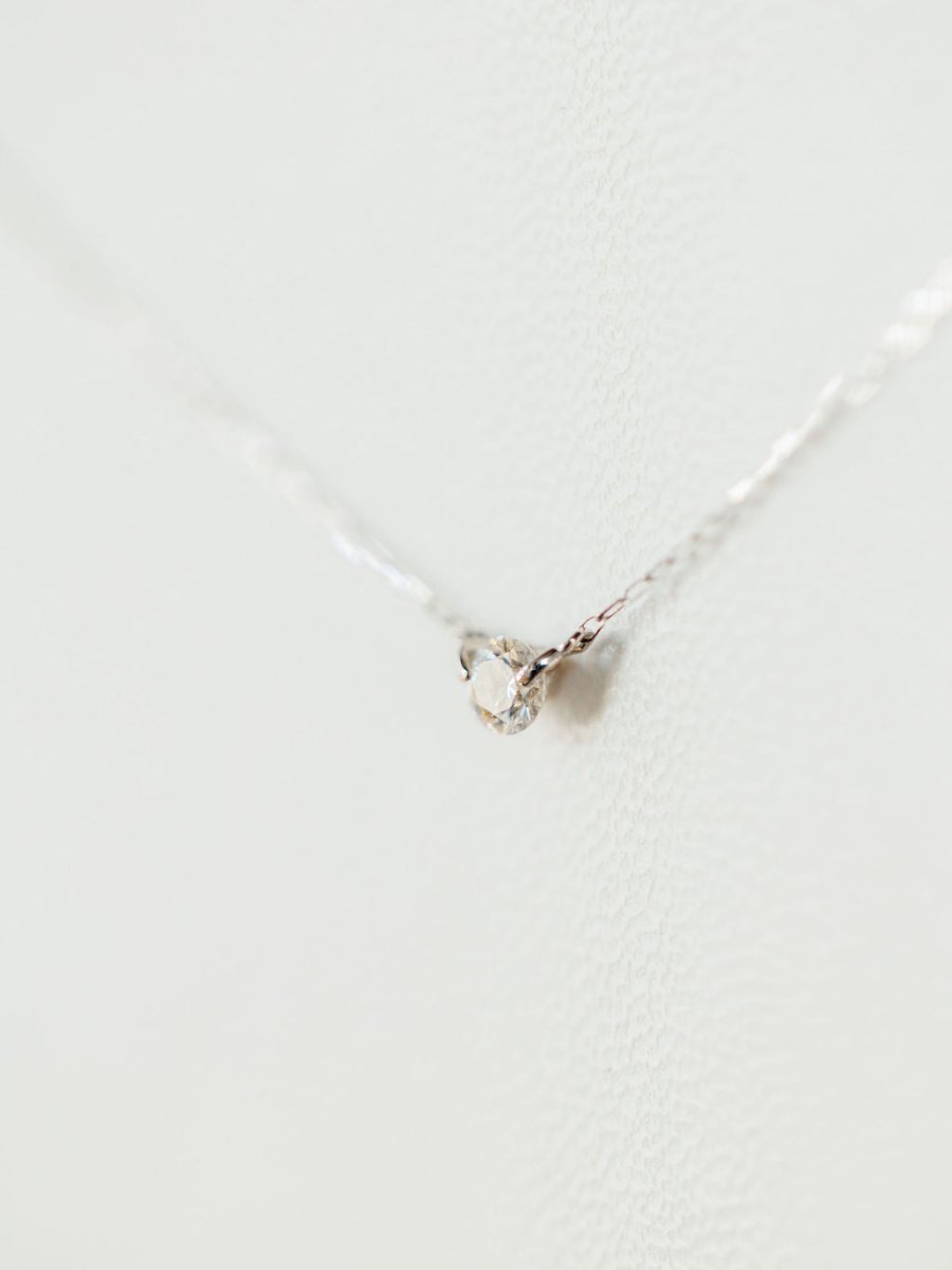 A close-up of the Petite Diamond Necklace {White Gold} by Savannah Sevens western life{&}style, featuring a delicate natural round diamond pendant, set against a softly textured white background.