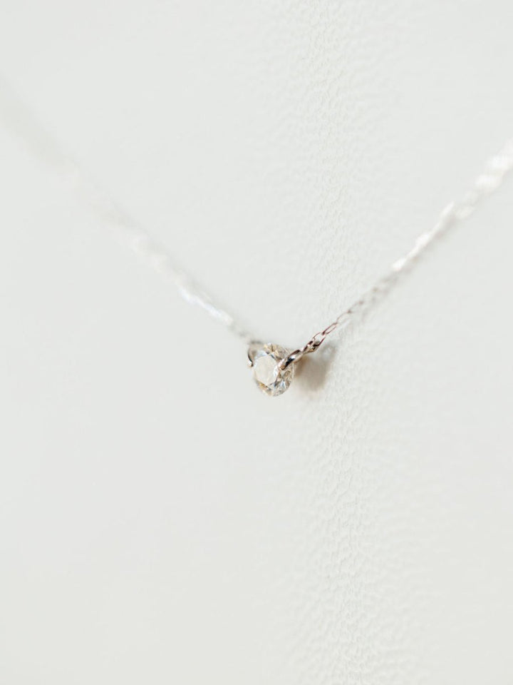 A close-up of the Petite Diamond Necklace {White Gold} by Savannah Sevens western life{&}style, featuring a delicate natural round diamond pendant, set against a softly textured white background.