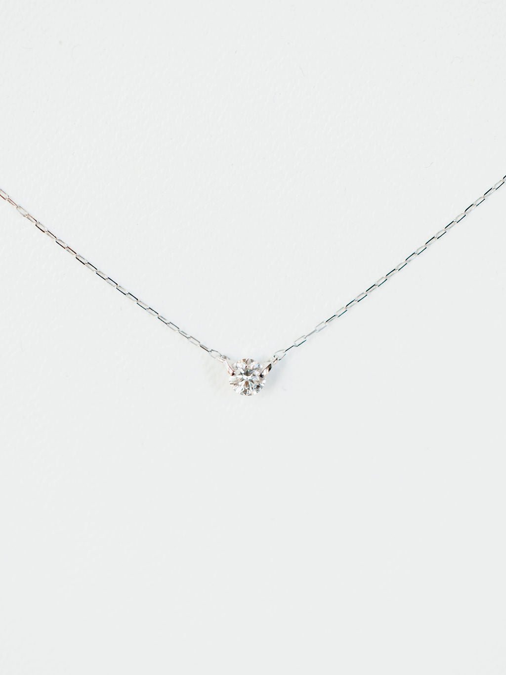 The Petite Diamond Necklace {White Gold} by Savannah Sevens western life{&}style features a delicate 18K white gold chain with a small natural round diamond pendant, displayed against a plain white background.