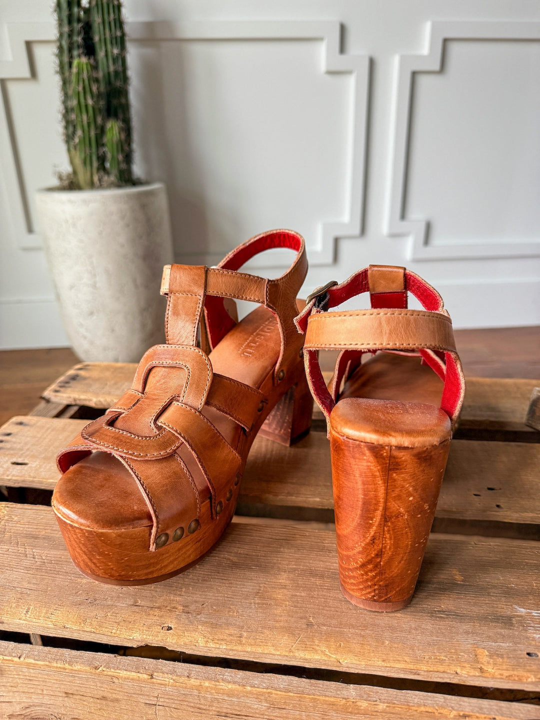 The Peyette by Savannah Sevens western life{&}style: tan leather strappy platform sandals with wooden heels, displayed on a pallet against a white textured wall and potted cactus. Made by BedStu. 