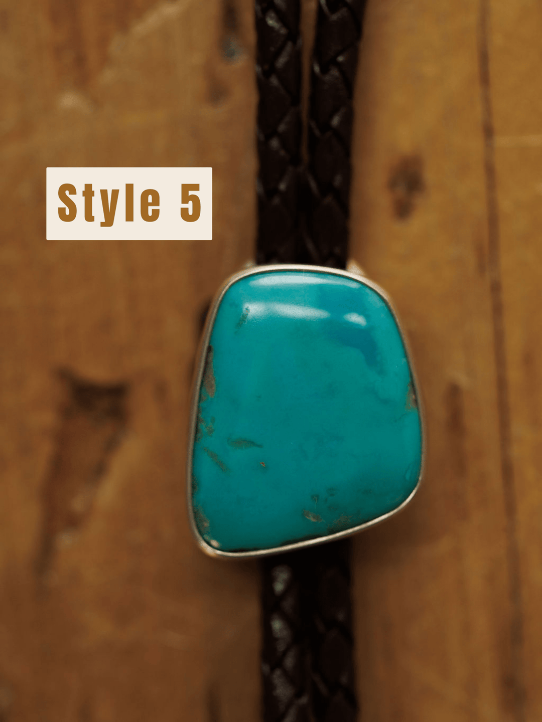 A close-up of the Savannah Sevens western life{&}style Peyote Bolo, a handmade turquoise bolo tie with braided dark brown cords, set against a wooden background. The text Style 5 appears on the left side.