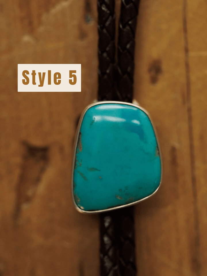 A close-up of the Savannah Sevens western life{&}style Peyote Bolo, a handmade turquoise bolo tie with braided dark brown cords, set against a wooden background. The text Style 5 appears on the left side.