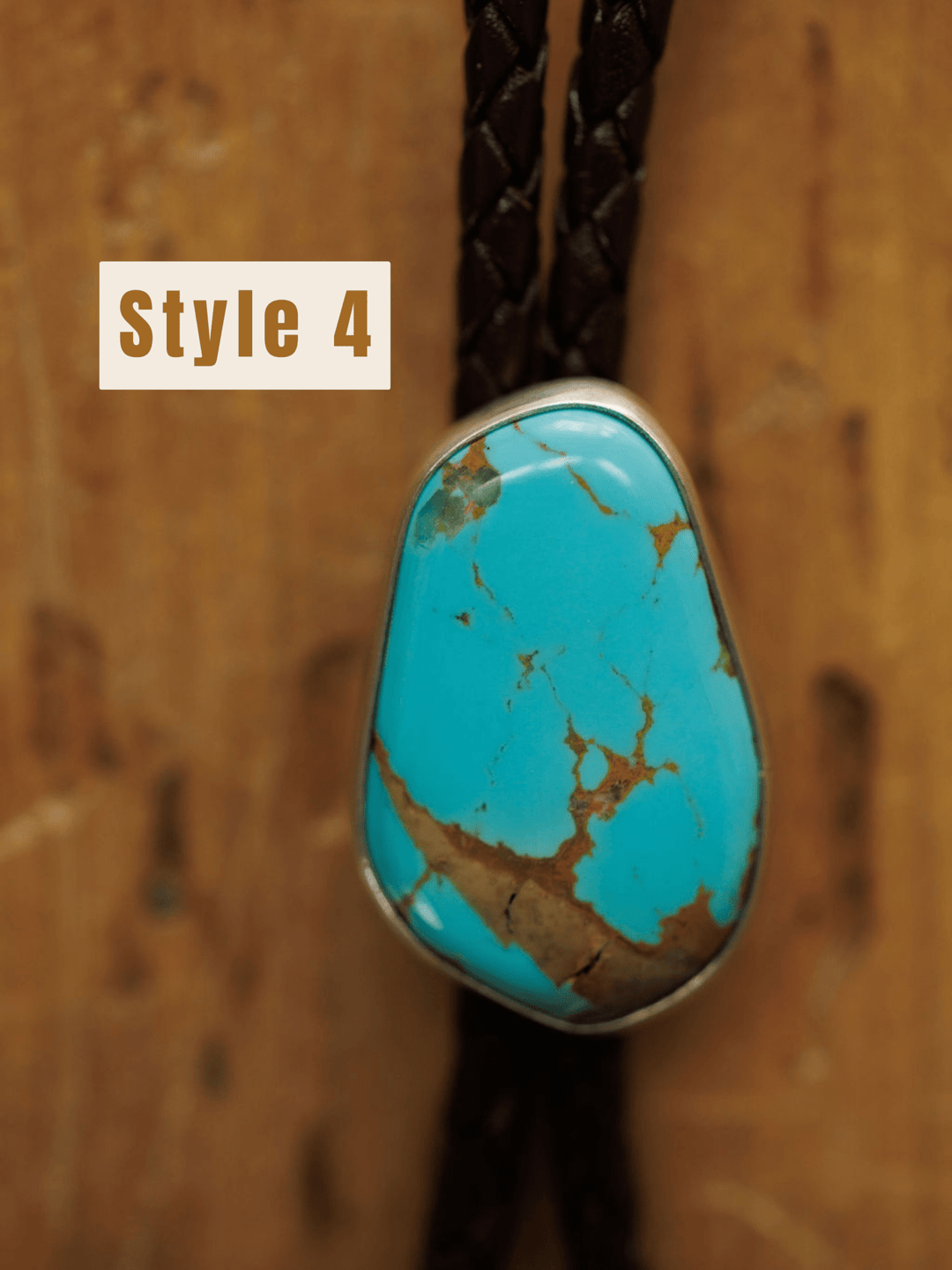 A close-up of the Peyote Bolo by Savannah Sevens western life{&}style, featuring a turquoise stone with brown veins set in silver on a braided dark cord. The text Style 4 appears in the upper left, with a wooden surface background.