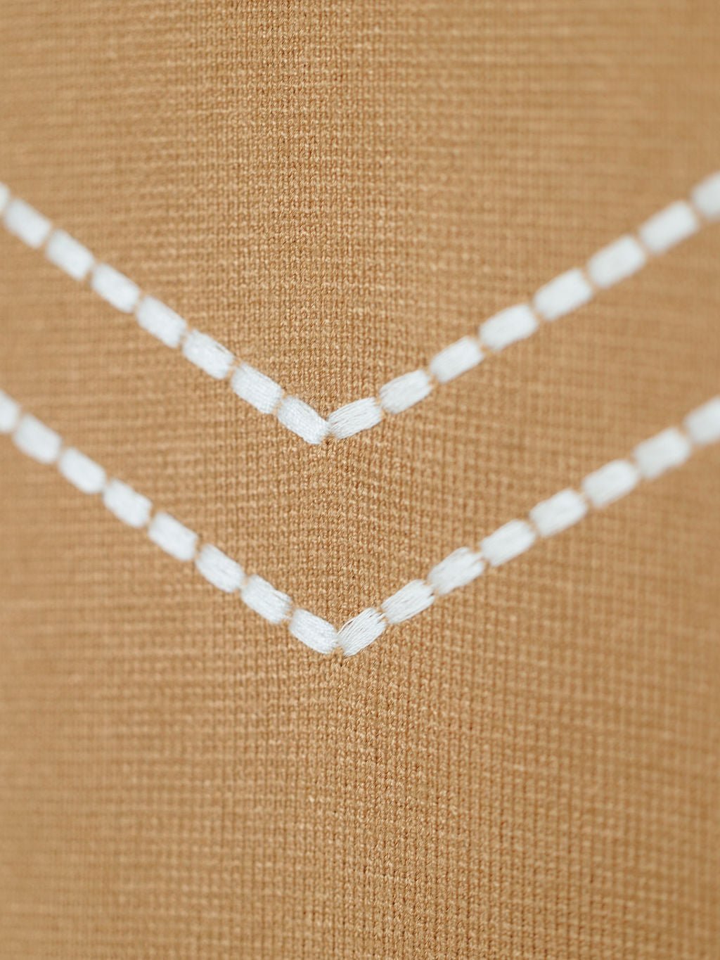 Close-up of the Platte Tan Stitch Dress by Savannah Sevens western life{&}style, featuring two white embroidered chevron details on soft tri-blend fabric with visible texture and stitching.