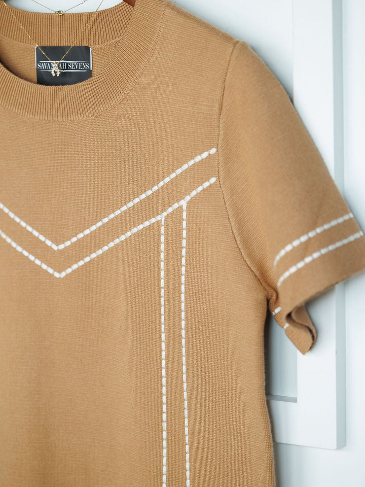 The Platte Tan Stitch Dress by Savannah Sevens western life{&}style features camel-colored tri-blend knit fabric with white geometric embroidered stitching on the front and sleeves, displayed on a hanger against a white background.