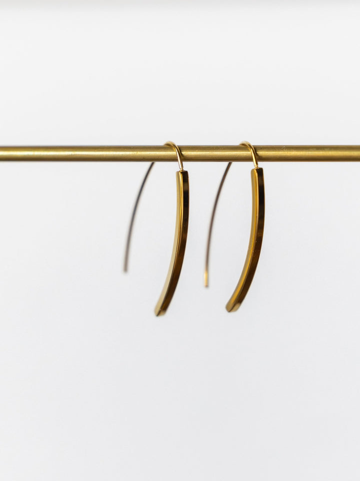 The Pondera Gold Earrings by Savannah Sevens western life{&}style hang on a thin gold rod against a white background. These waterproof, hypoallergenic earrings deliver elegant, minimalist style perfect for everyday wear.