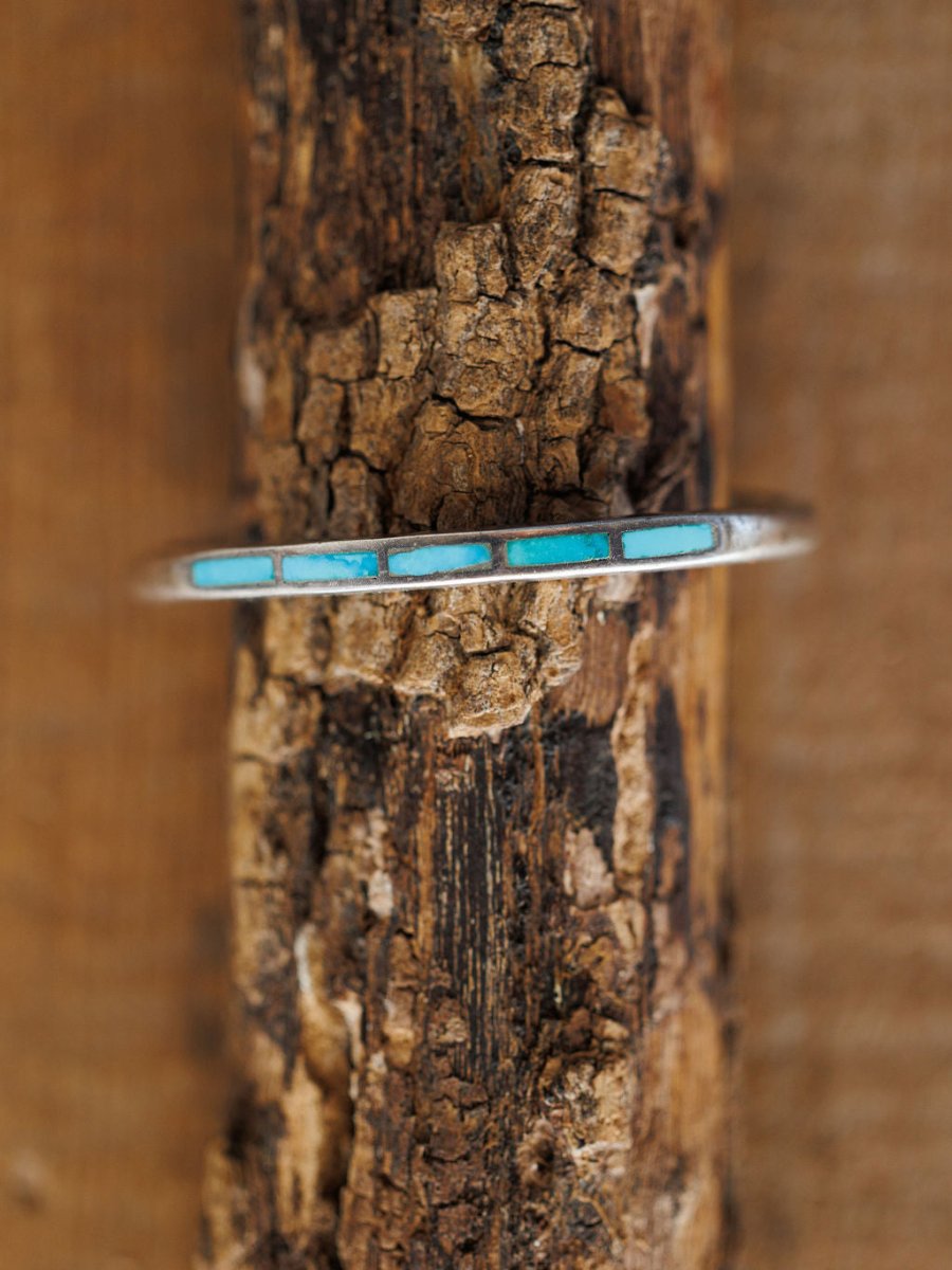 The Ponderosa Cuff by Savannah Sevens western life{&}style, a silver bracelet featuring five rectangular turquoise inlays, is displayed vertically on textured wood with a brown background.