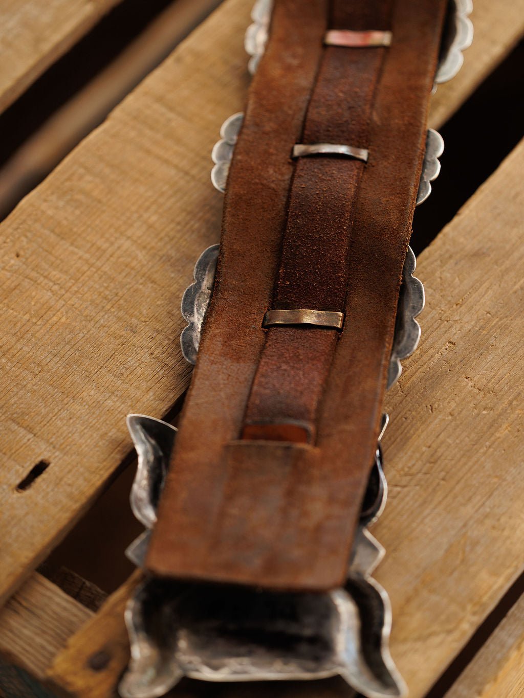 Close-up of the Portales Belt by Savannah Sevens western life{&}style, showing the back side with textured leather and silver metal loops, set on a wooden surface.