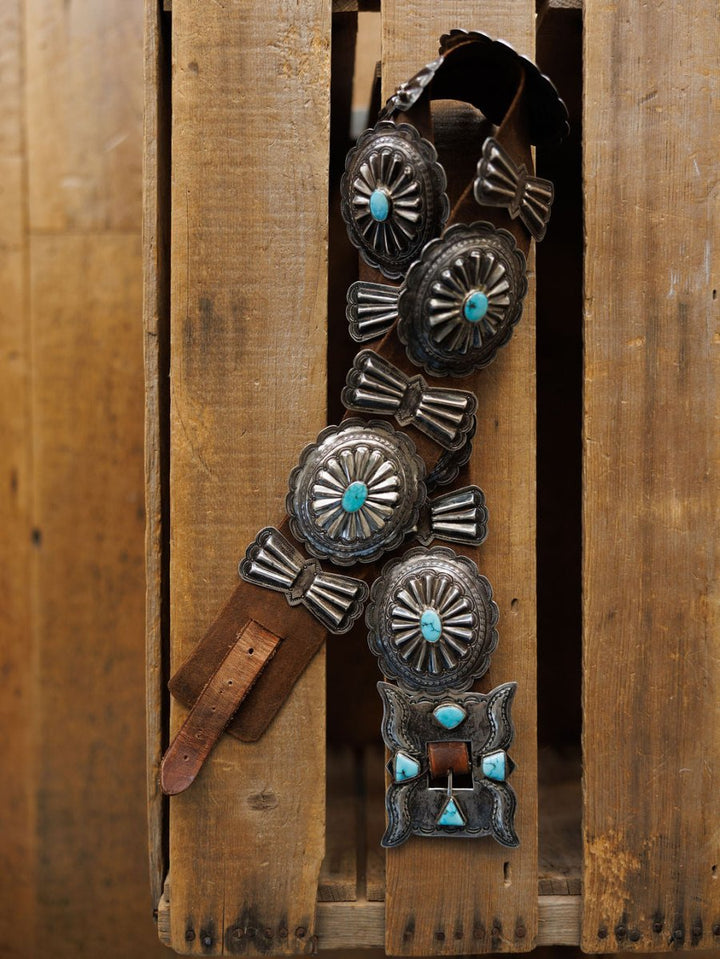 The Portales Belt by Savannah Sevens western life{&}style features large turquoise conchos and Navajo handmade leather, displayed on a rustic wooden surface.