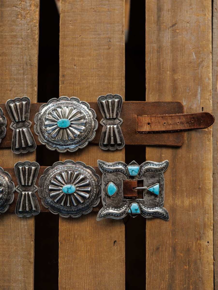 The Portales Belt by Savannah Sevens western life{&}style features large, ornate sterling silver conchos with #8 Turquoise stones and a rectangular buckle, shown on a wooden surface.