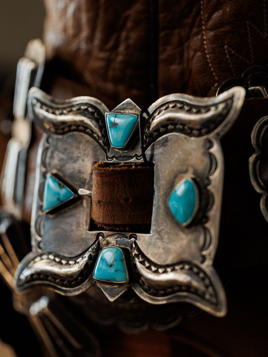 A close-up of the Portales Belt by Savannah Sevens western life{&}style, showcasing a vintage sterling silver buckle with four turquoise stones in a symmetrical design on a brown Navajo handmade leather belt.