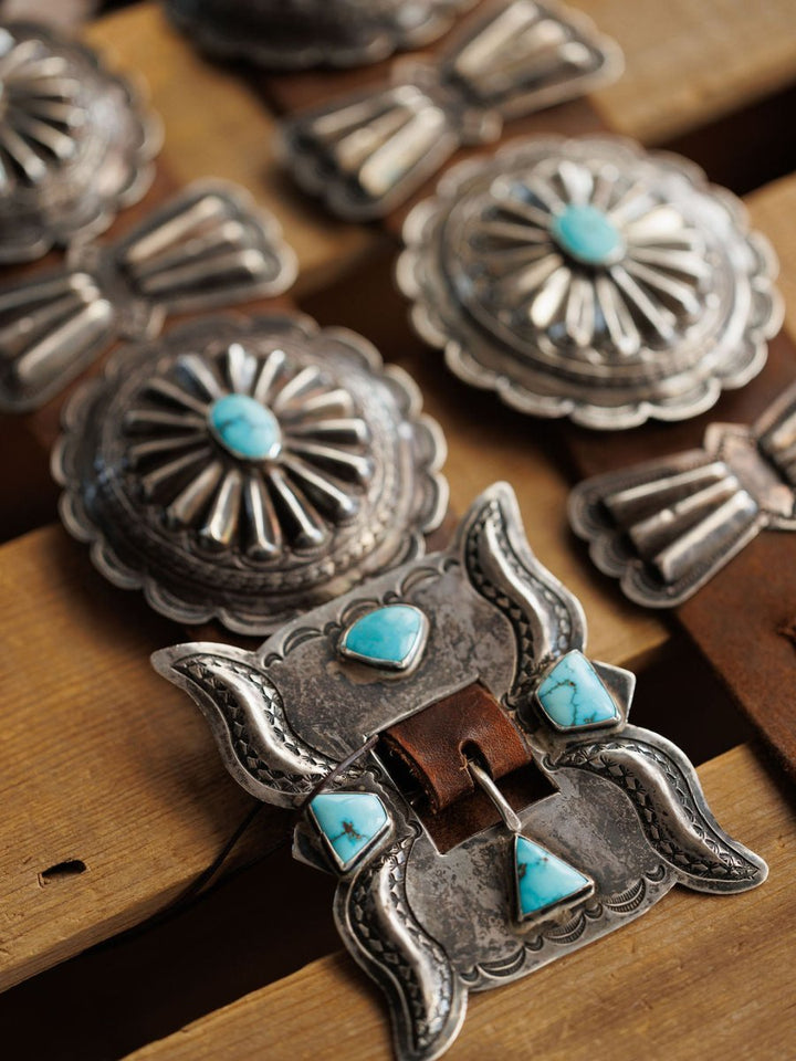 Close-up of the Portales Belt by Savannah Sevens western life{&}style, a vintage sterling silver belt with #8 Turquoise stones, detailed engraving, and scalloped shapes, shown on a wooden surface.