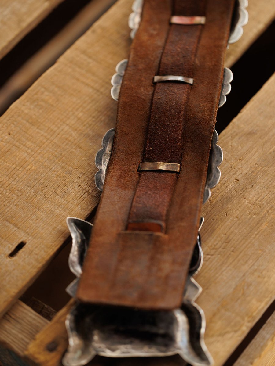 Close-up of the Portales Belt by Savannah Sevens western life{&}style, showing the back side with textured leather and silver metal loops, set on a wooden surface.