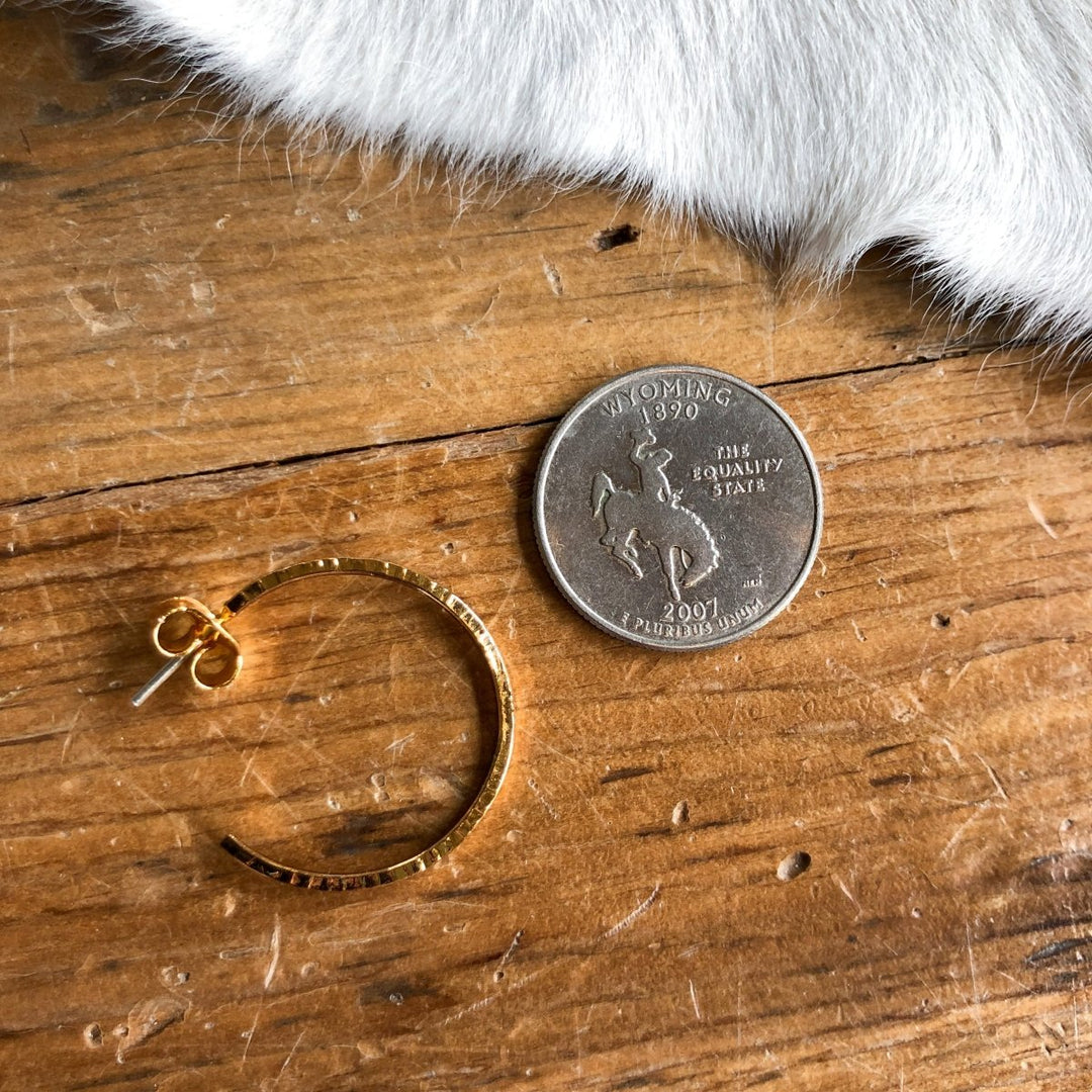 A Posen Earring by Savannah Sevens western life{&}style and a 2007 Wyoming state quarter rest on wood beside light-colored cowhide.