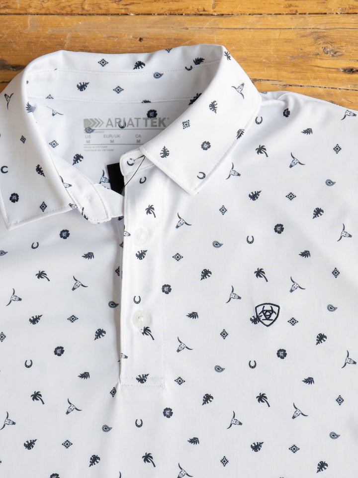 The Prescott Ariat Men's Western Graphic Polo by Savannah Sevens western life{&}style is a white shirt with black palm trees, horseshoes, and tropical drinks. It offers moisture-wicking comfort and is neatly displayed on a wooden surface.