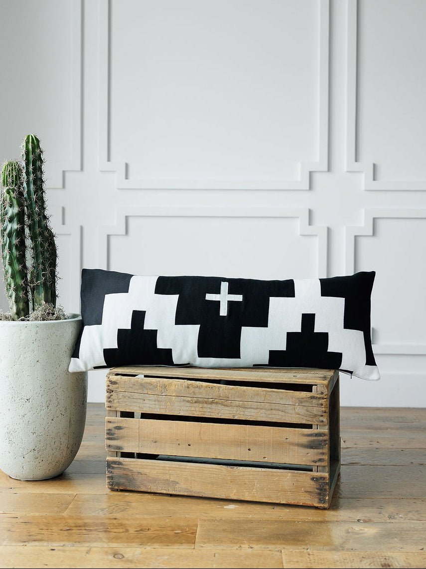 The Presidio Lumbar Pillow Cover {B & W} by Savannah Sevens western life{&}style is displayed on a wooden crate beside a cactus, set against a white paneled wall.
